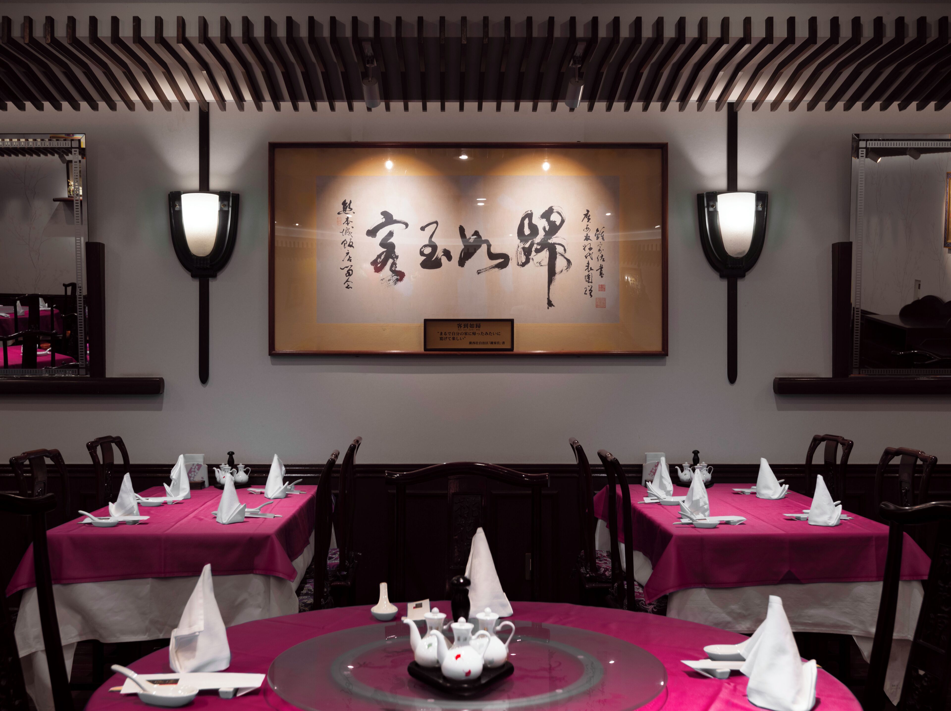 Un restaurant où les tables sont dressées pour le service, avec une grande œuvre calligraphique encadrée qui orne le mur.