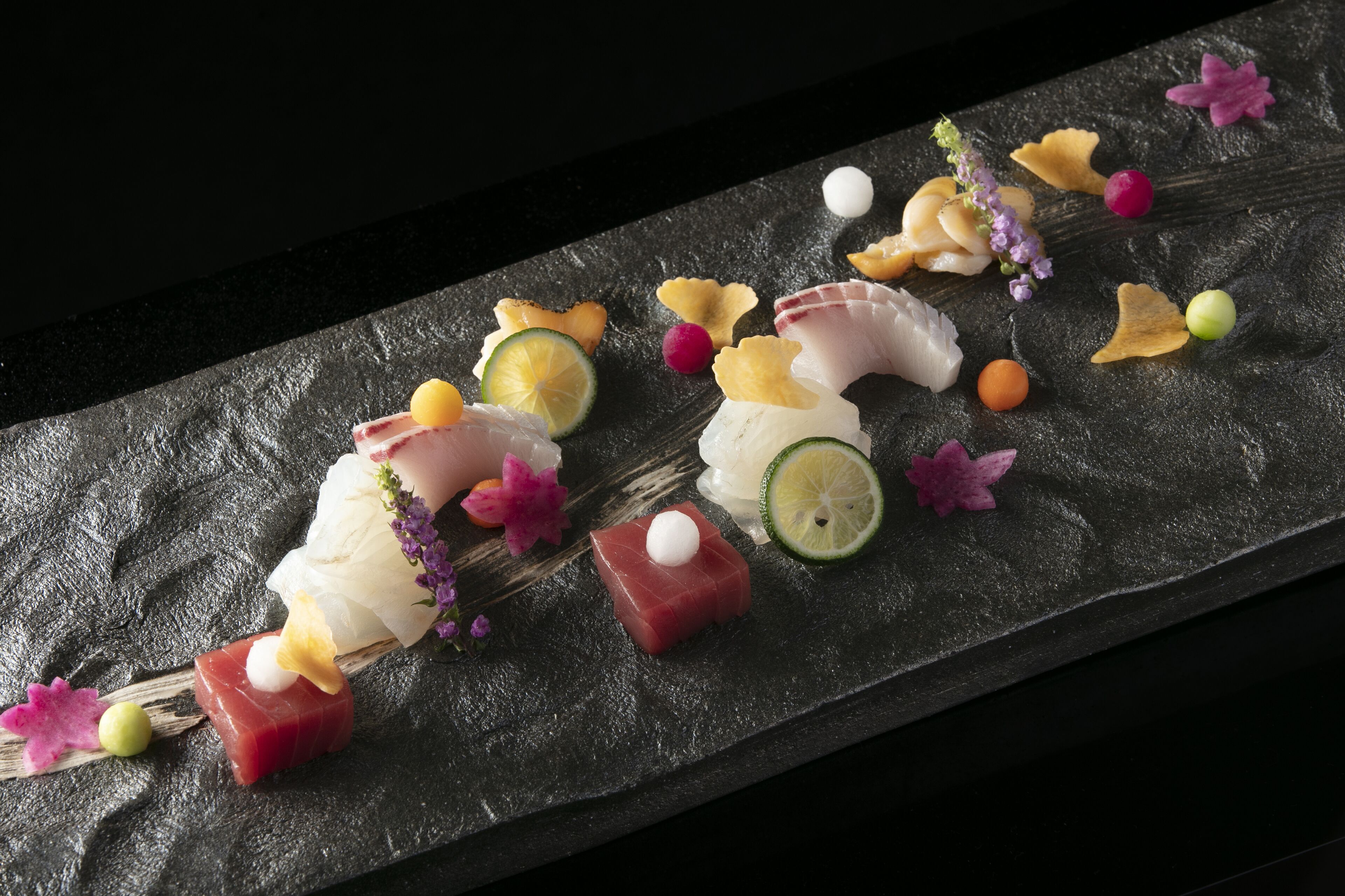 A variety of sushi pieces on a slate serving board, accompanied by decorative elements like flowers and citrus slices.