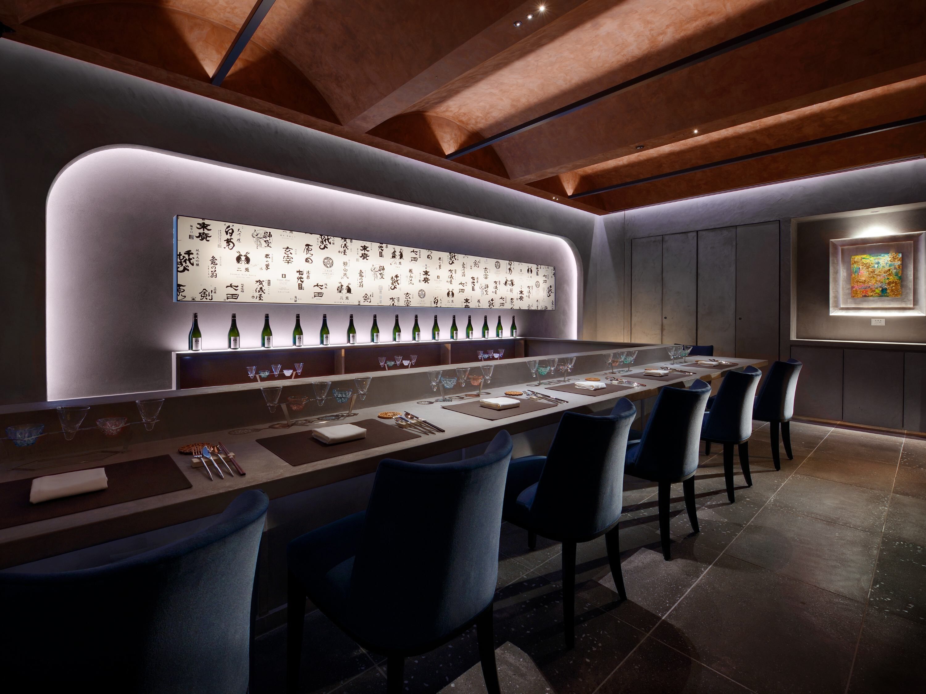 A modern bar with a long counter, multiple seating options, and a wall of decorative items.