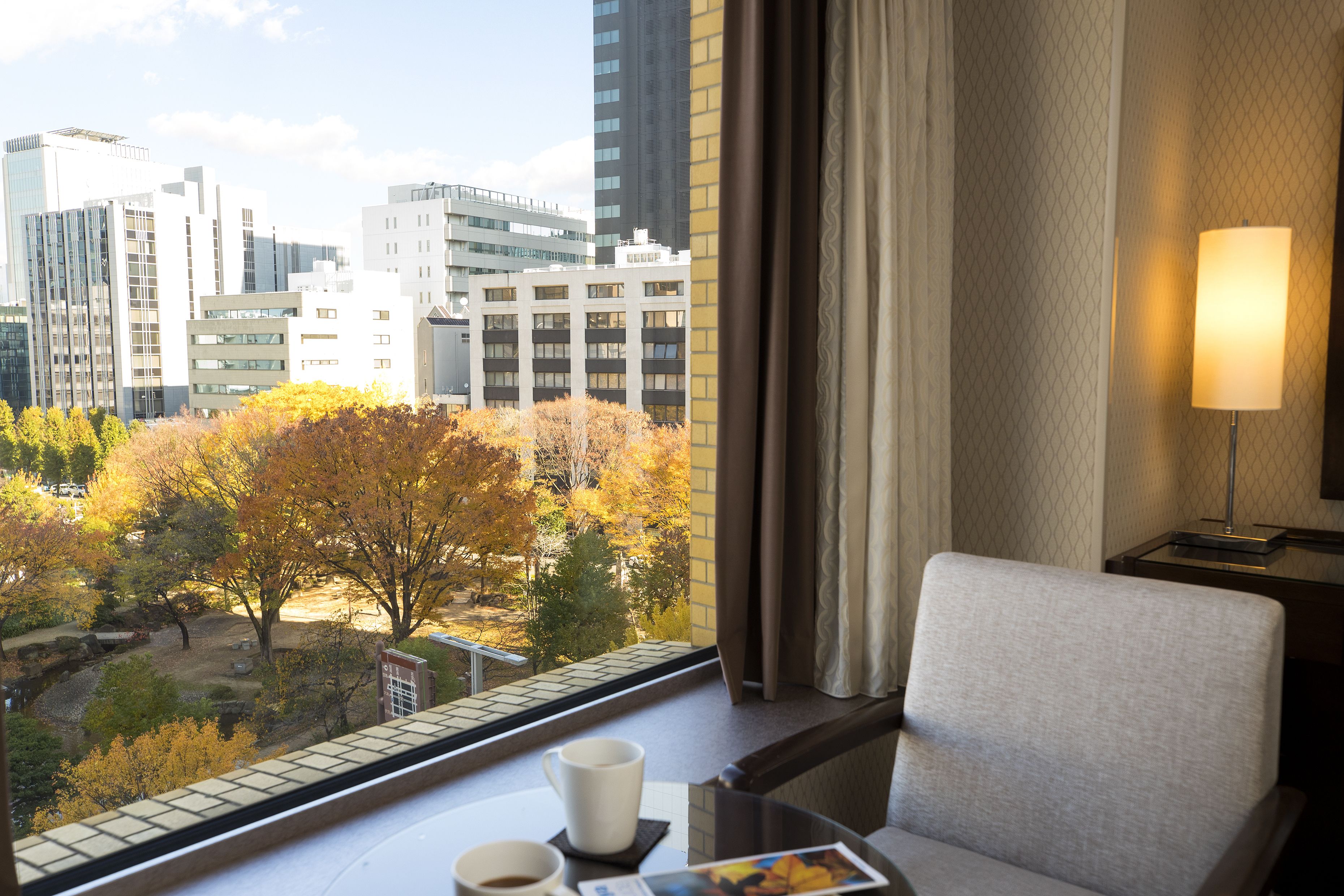 A hotel room with a view of autumn trees and city buildings.