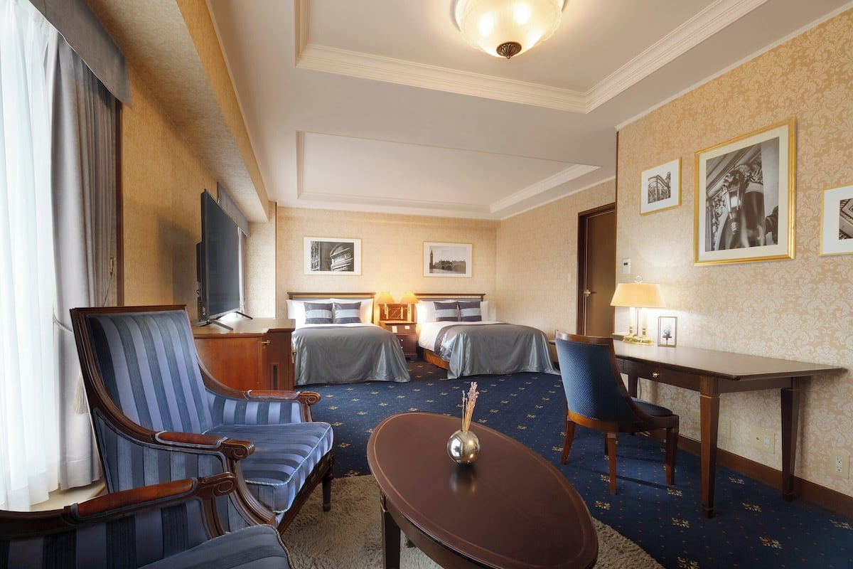Une chambre d’hôtel avec un lit, deux fauteuils, une petite table, un téléviseur et des tableaux encadrés au mur.