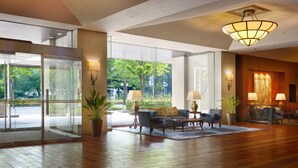 A spacious lobby with a wooden floor, a seating area with sofas and armchairs, a large window offering a view of greenery, and a chandelier. - Nagoya Kanko Hotel (Nagoya)