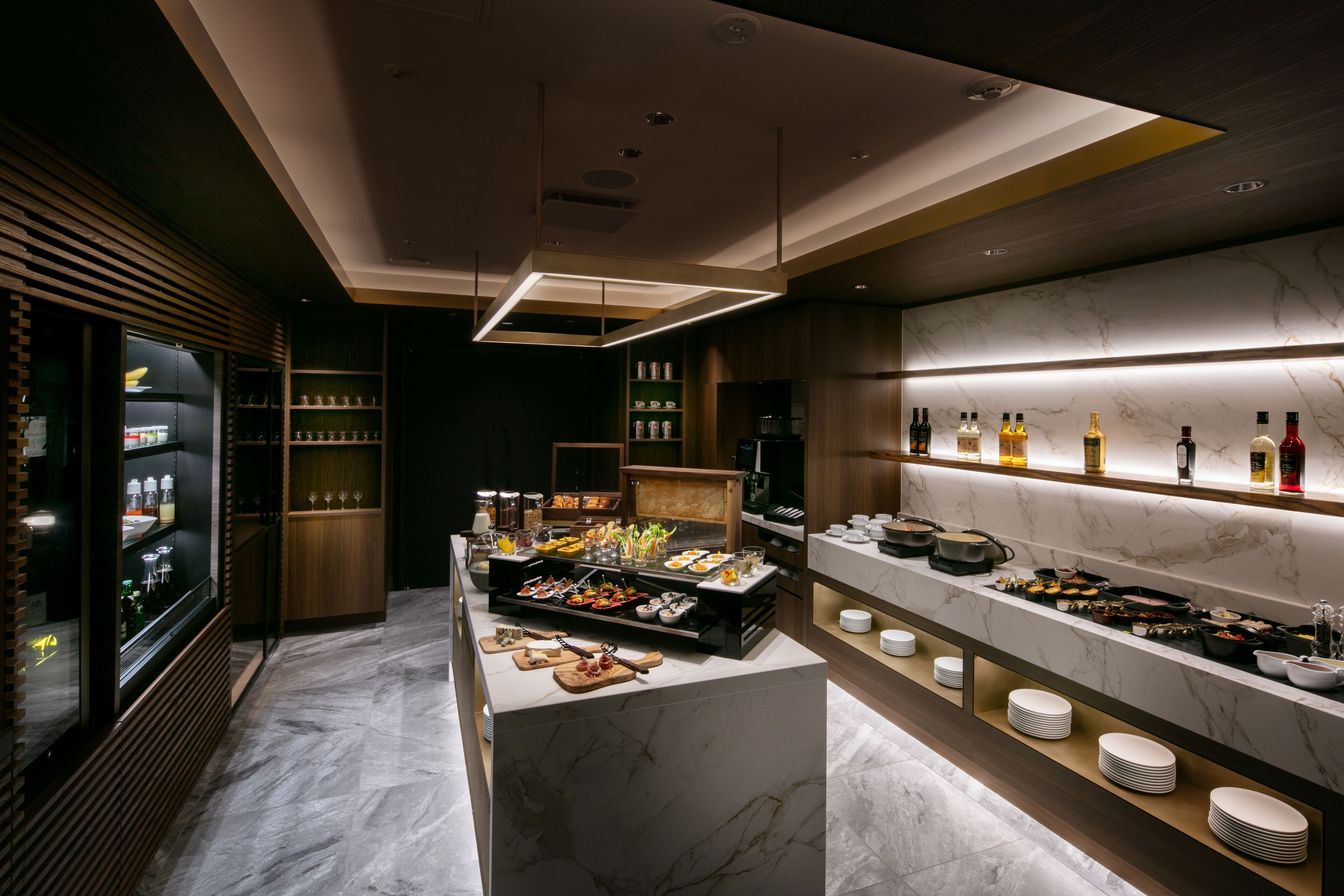 A modern kitchen with marble countertops, a central island with food, and a wine rack.