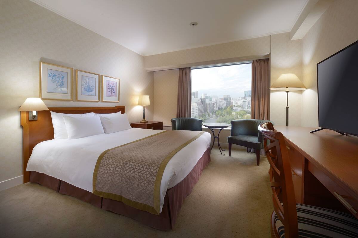 Une chambre d’hôtel avec un grand lit, un bureau, une chaise, une télévision et une vue sur la ville.