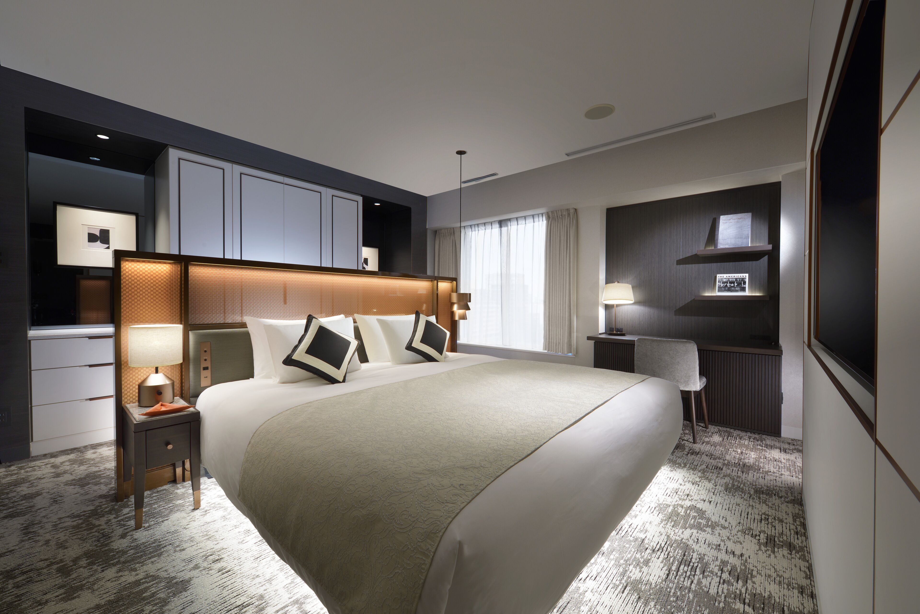 A modern hotel room with a large bed, bedside tables, a desk, and a TV.