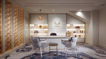 Un espace d’accueil moderne avec un comptoir en marbre, deux chaises blanches et un mur décoratif orné de motifs géométriques.