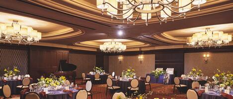 A banquet hall with round tables, chairs, chandeliers, and a grand piano.