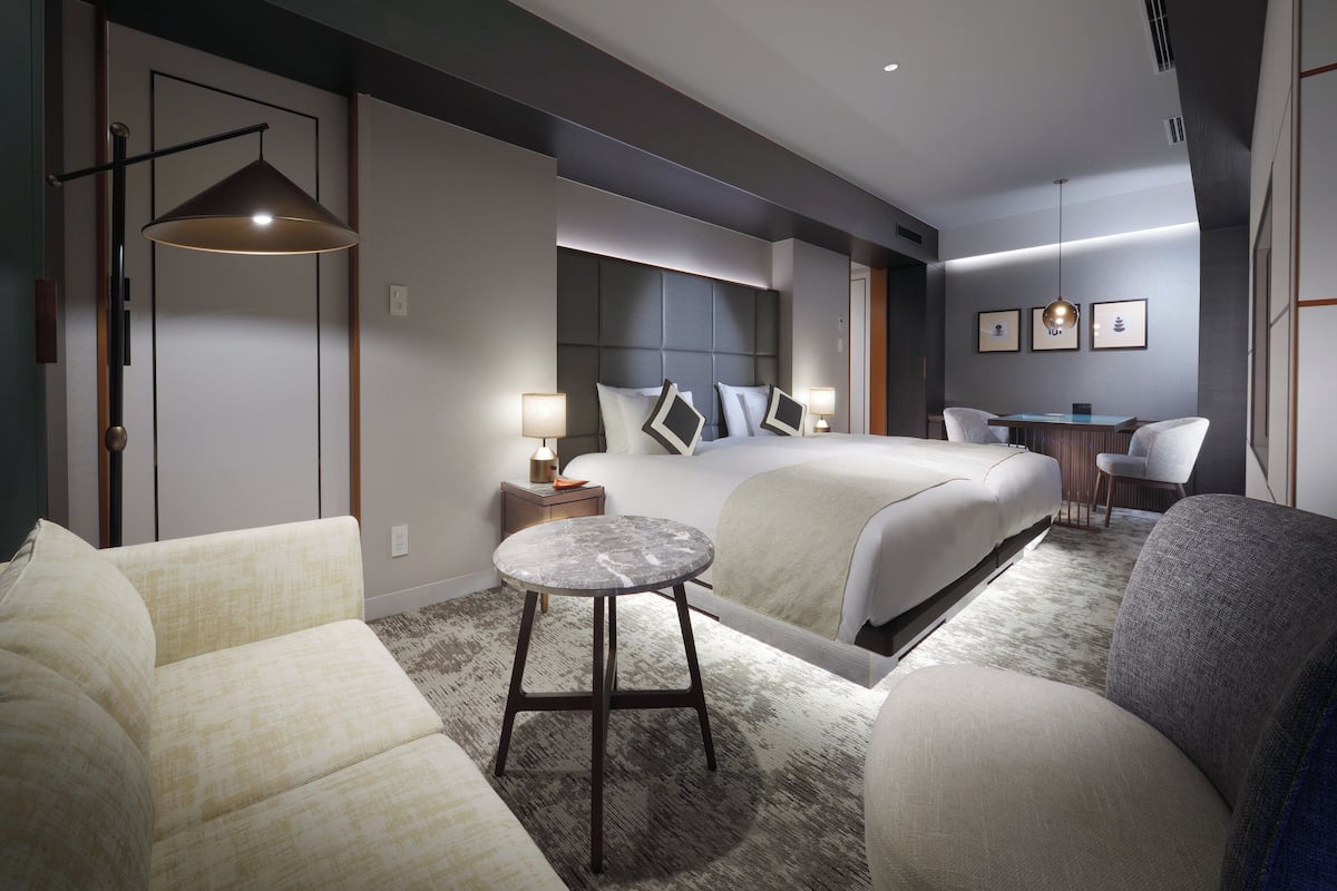Une chambre d’hôtel moderne dotée d’un grand lit, d’un coin salon avec un canapé et un fauteuil, d’une petite table ronde et d’un bureau avec une chaise.