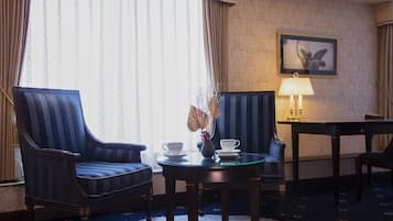 A hotel room with two upholstered armchairs, a small round table with a vase and a cup, and a lamp on a side table.