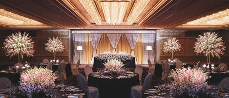 A formal dining room with round tables, floral centerpieces, and elegant lighting fixtures.