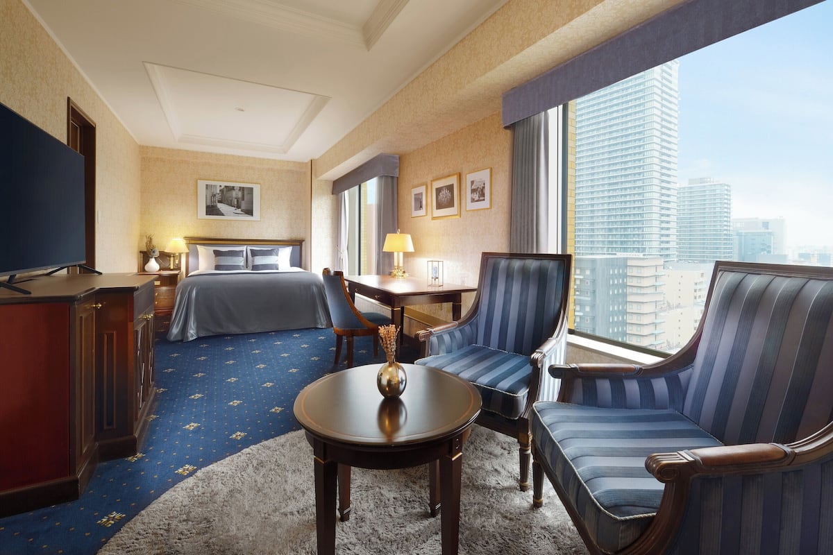 Une chambre d’hôtel avec un lit, un bureau, une chaise, une télévision et une vue sur la ville.