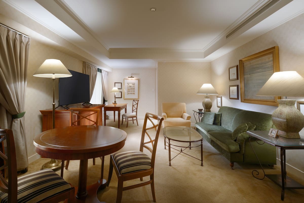 Un salon bien éclairé, avec une table ronde en bois, deux chaises, un canapé et un téléviseur.