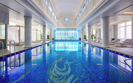 A large indoor swimming pool with a tiled floor, surrounded by columns and seating areas.
