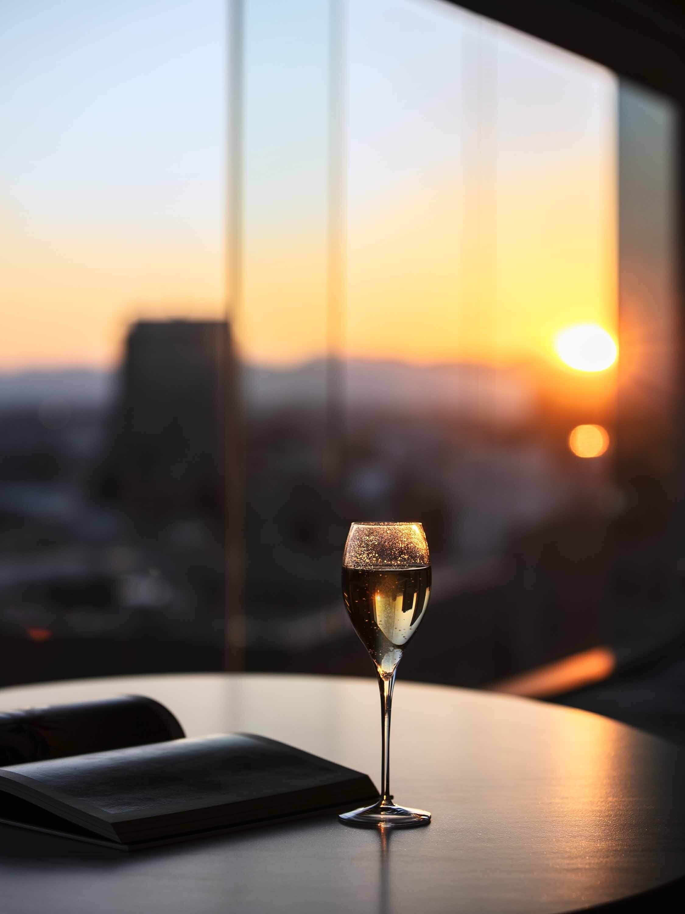 Una copa de champán sobre una mesa, con vista a un paisaje urbano al atardecer.