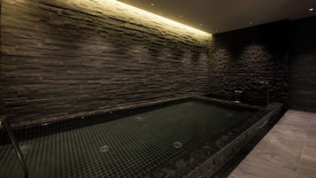 A spa area with a stone wall, a tiled floor, and a rectangular hot tub.