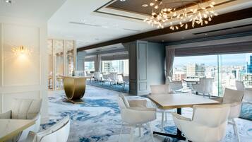A modern hotel lobby with a large dining area, seating arrangements, and a city view through large windows.
