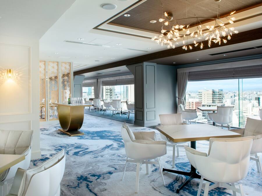 A modern hotel lobby with a large dining area, seating arrangements, and a city view through large windows.