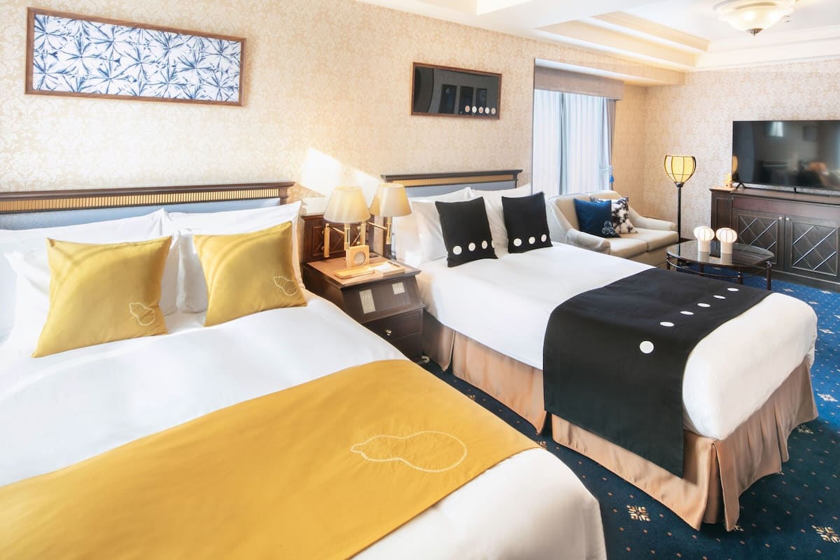 Une chambre d’hôtel avec deux lits, un canapé, une télévision et un bureau avec des lampes.