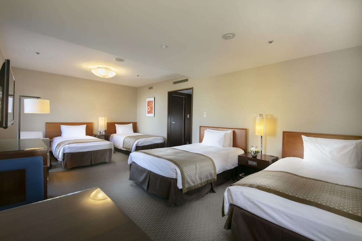 Une chambre d’hôtel avec quatre lits, un bureau, une chaise et un téléviseur.