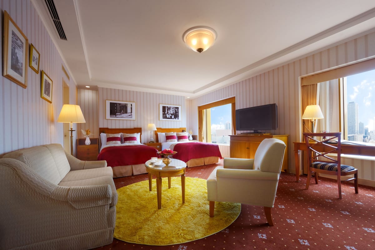 Une chambre d’hôtel comprenant un lit, deux fauteuils, un canapé, une télévision et une fenêtre donnant sur la ville.