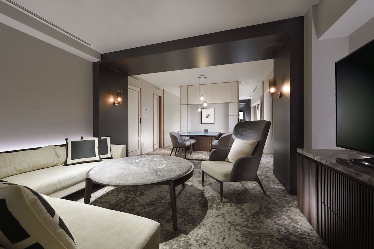 Une chambre d’hôtel moderne équipée d’un canapé, d’un fauteuil, d’une table ronde et d’un téléviseur.