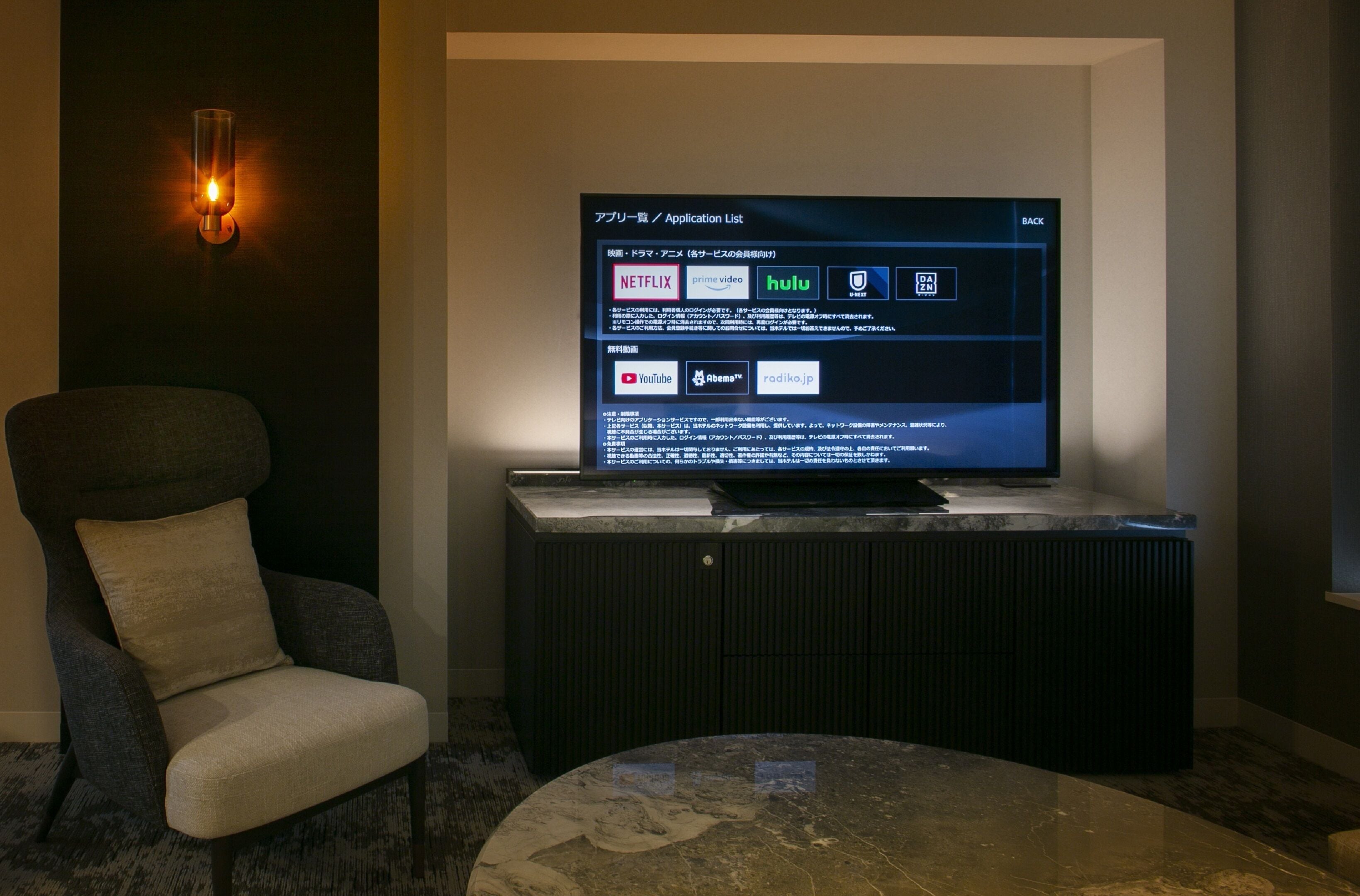 A modern living room with a flat-screen TV displaying an application list, a comfortable armchair, and a marble coffee table.