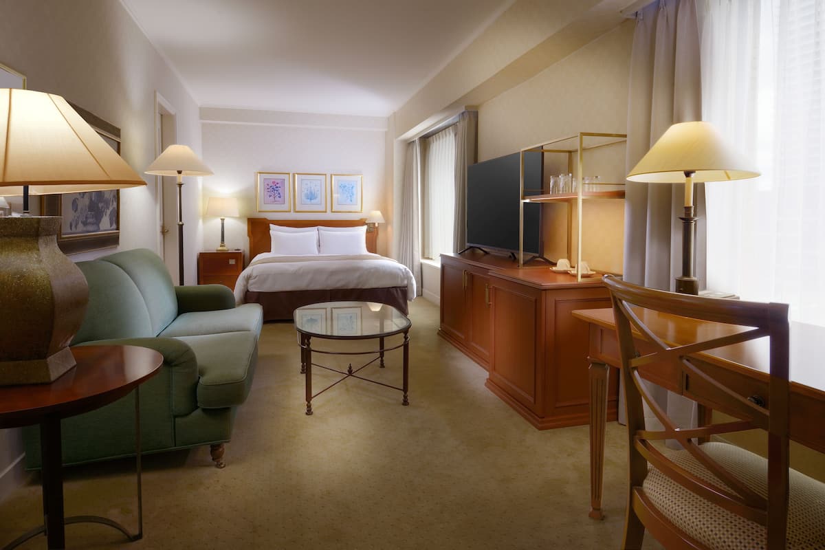 Une chambre d’hôtel avec un lit, un canapé vert, une petite table, un bureau en bois, une télévision et deux lampes.