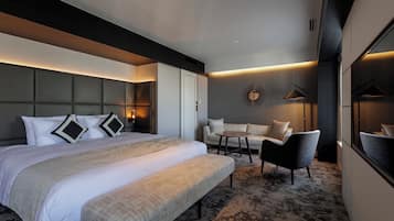 A modern hotel room with a large bed, a sofa, a small table, and a bench.