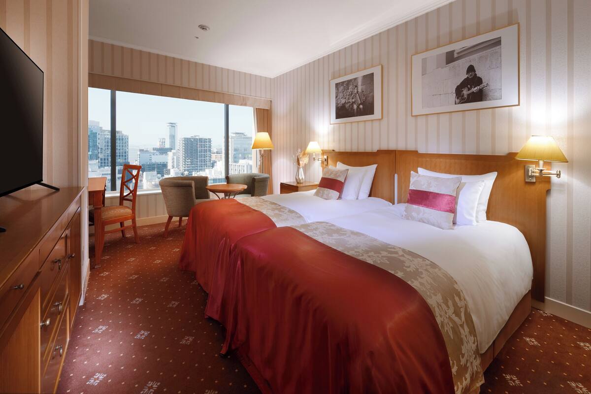 Une chambre d’hôtel avec un grand lit, deux tables de chevet, un bureau avec une chaise, une télévision et une vue sur le paysage urbain.