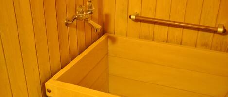 Una bañera de madera con un cabezal de ducha de vidrio y una barra de apoyo metálica.