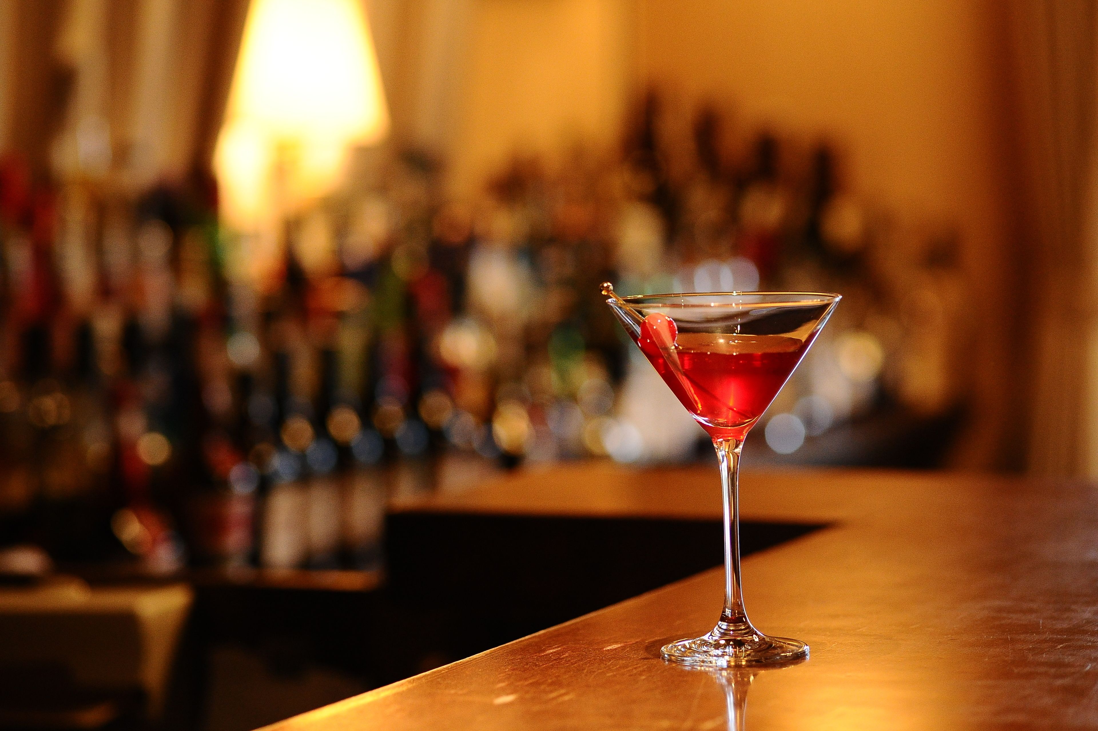 A martini glass with a red drink on a bar counter.