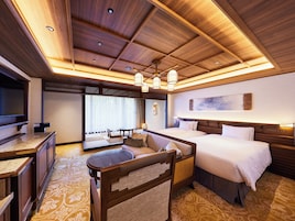 Habitación de hotel con techo de madera, una cama, un sofá, un televisor y una zona de comedor.