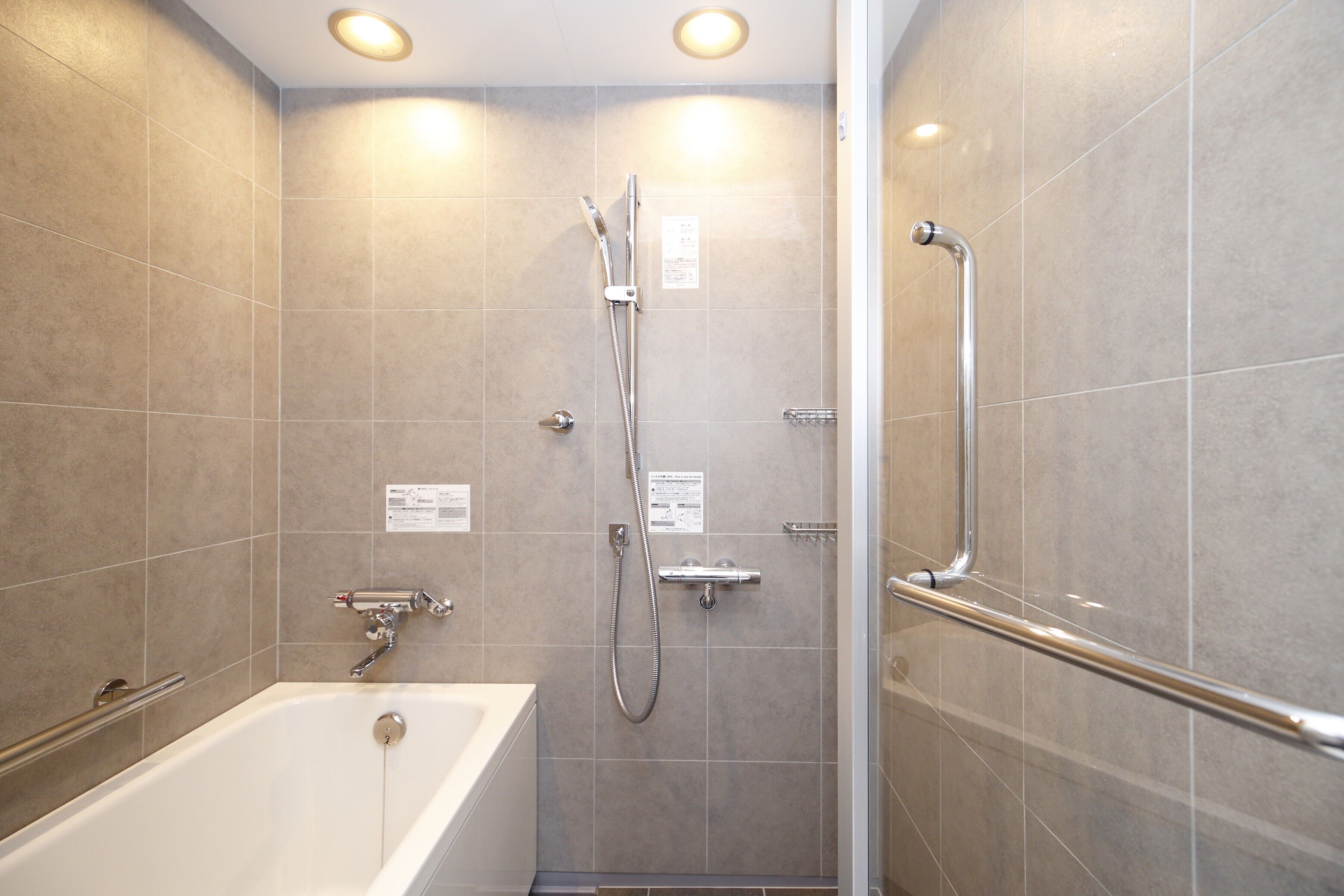 A modern bathroom with a bathtub, shower, and handrails.