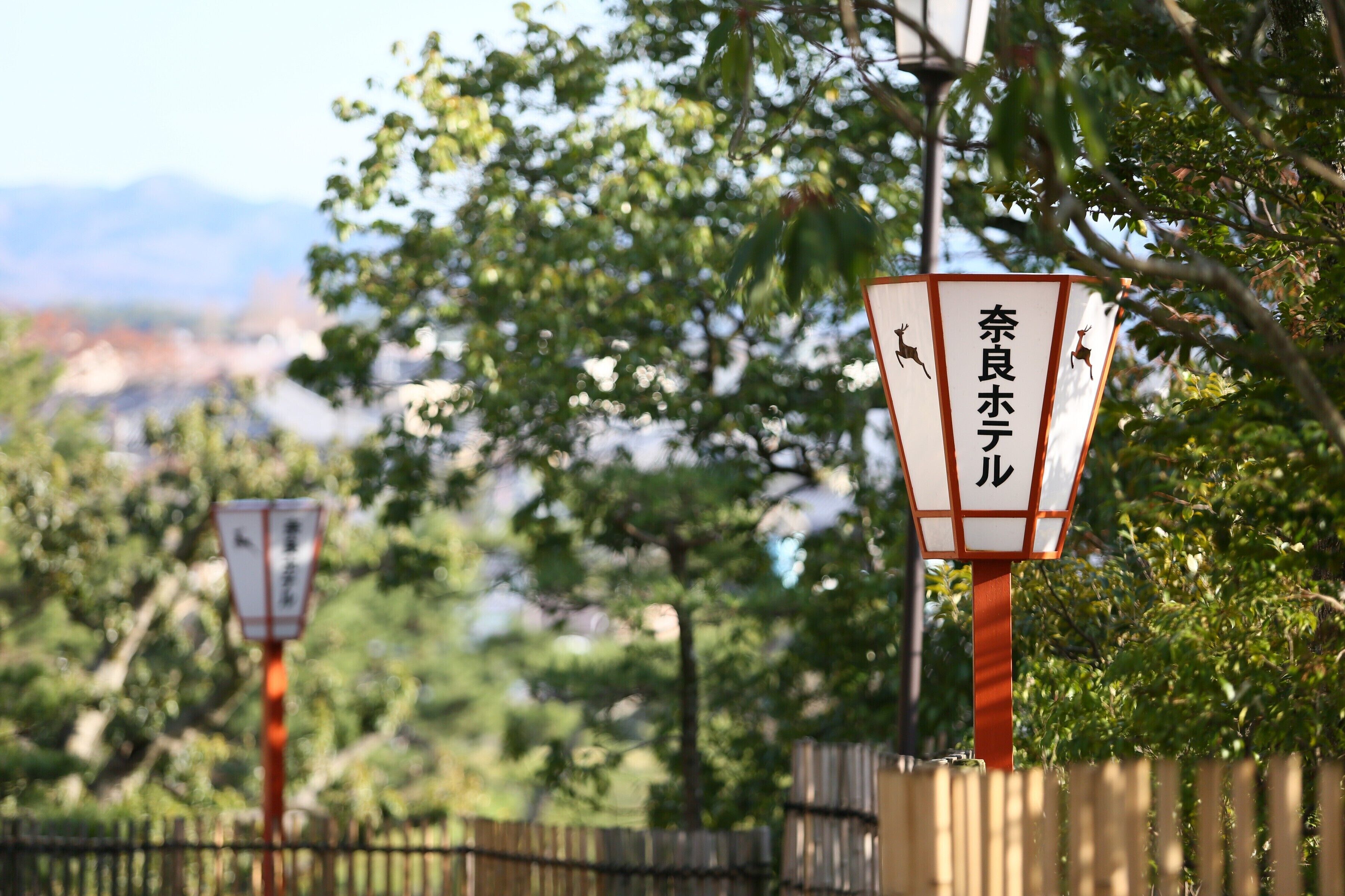 Zwei traditionelle japanische Laternen mit Hirschmotiven vor sattem Grün und fernen Bergen.