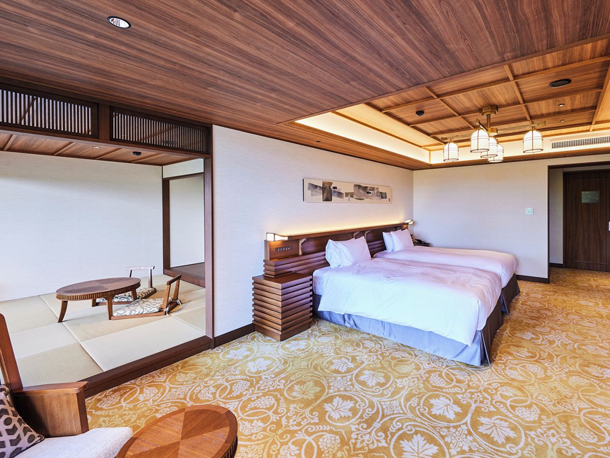 A hotel room with a bed, a seating area with a table, and a large mirror.
