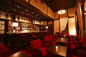 A bar area with a long counter, multiple seating options, and a chandelier.