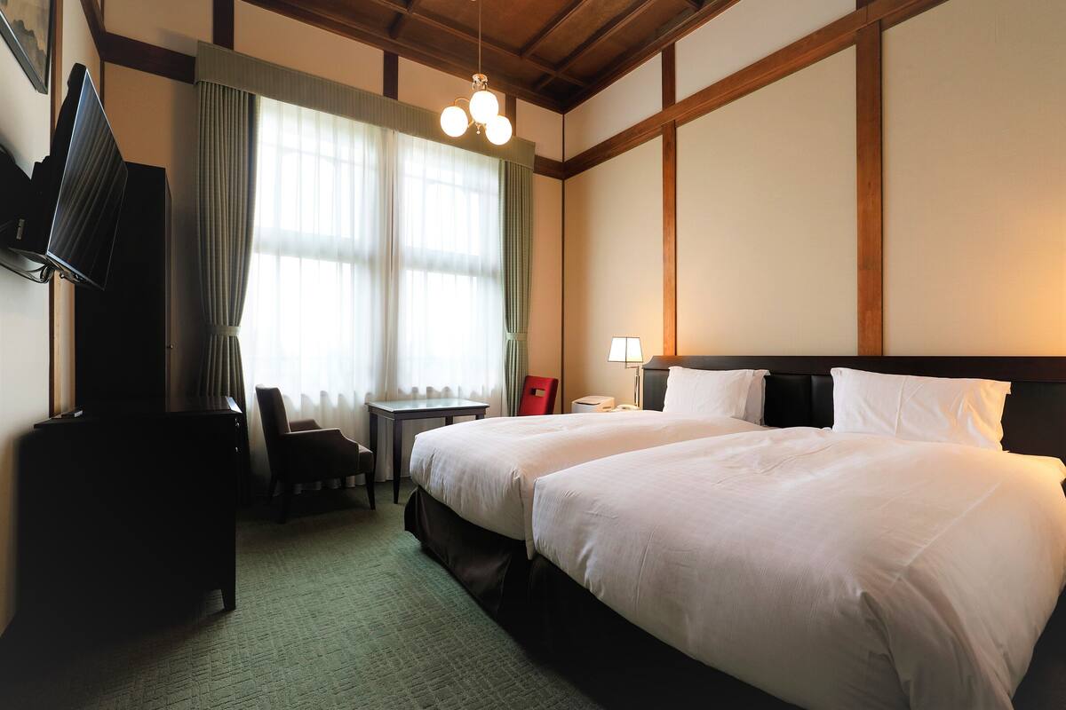 A hotel room with a large bed, a desk, a chair, a television, and a lamp.