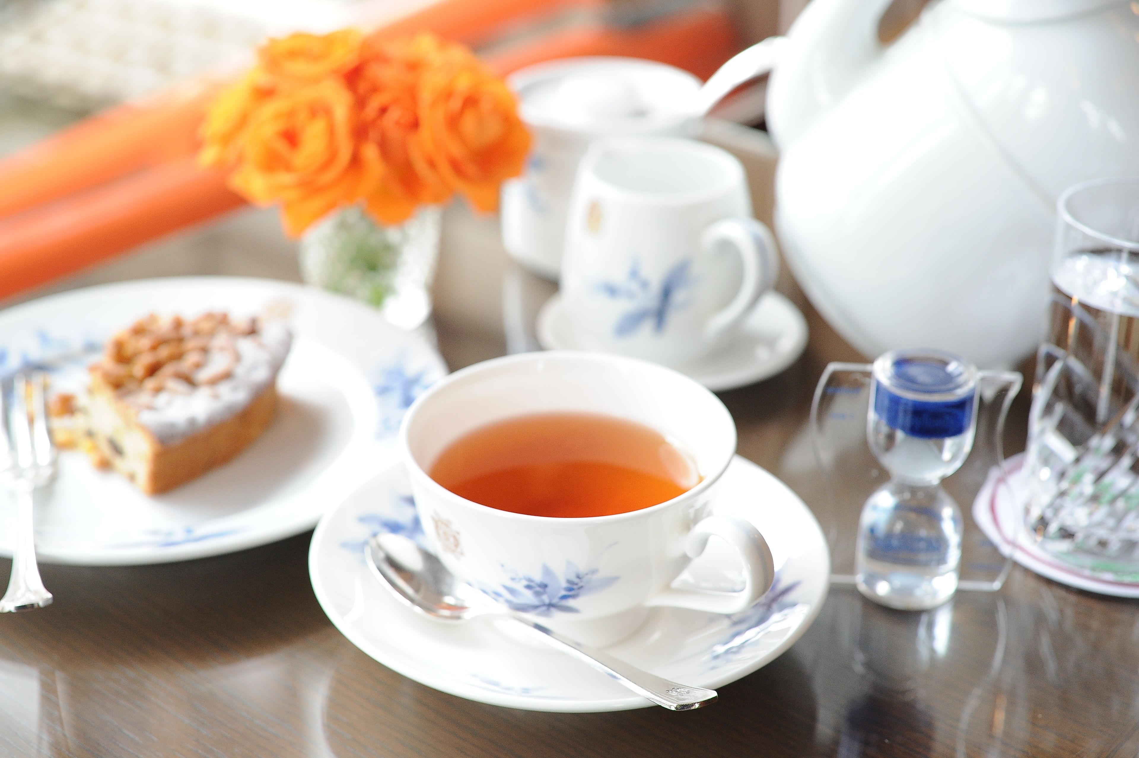 Ein Tisch gedeckt mit einer Teetasse, einem Kuchenstück, einem Teekessel, einer Zuckerdose und einer Vase mit Blumen.