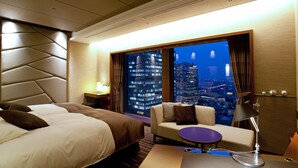 A hotel room with a bed, a sofa, a small table, a lamp, and a large window with a city view. - Hotel Granvia Osaka (Osaka)