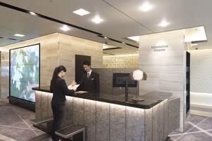 A reception desk with a digital screen, a man in a suit, and a woman in business attire.