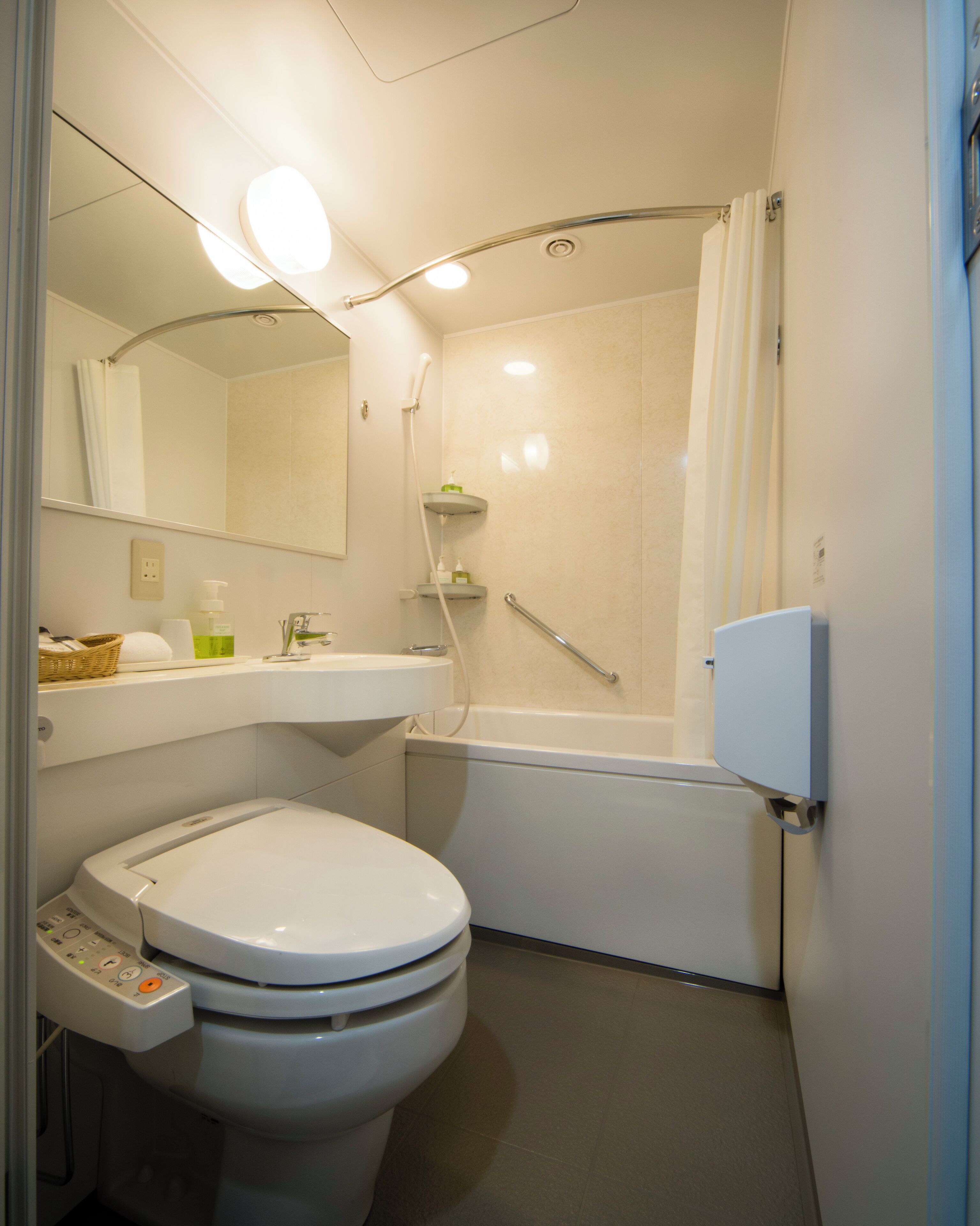 A compact bathroom with a toilet, a sink, a shower, and a mirror.