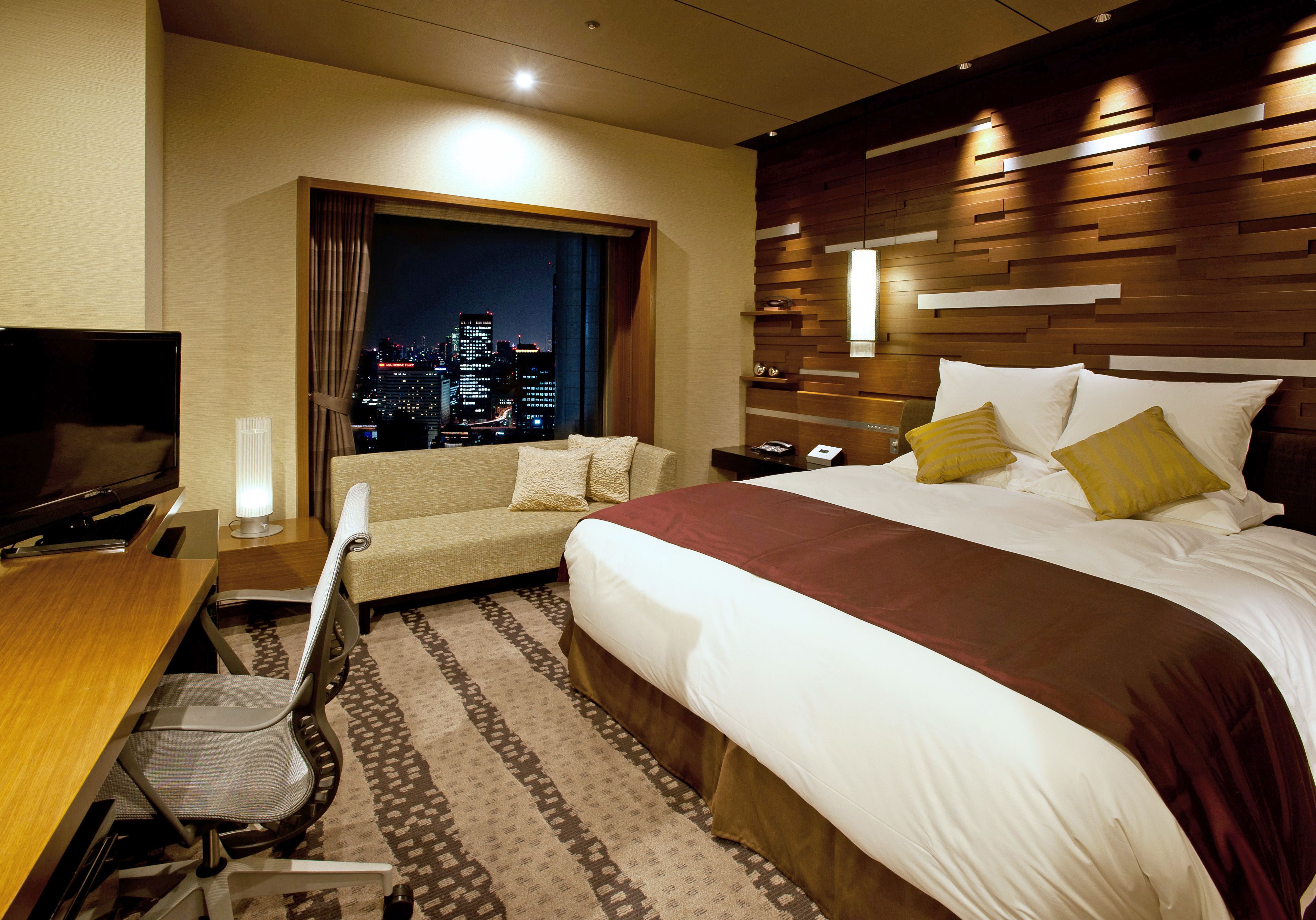 A hotel room with a bed, a sofa, a desk, and a TV.