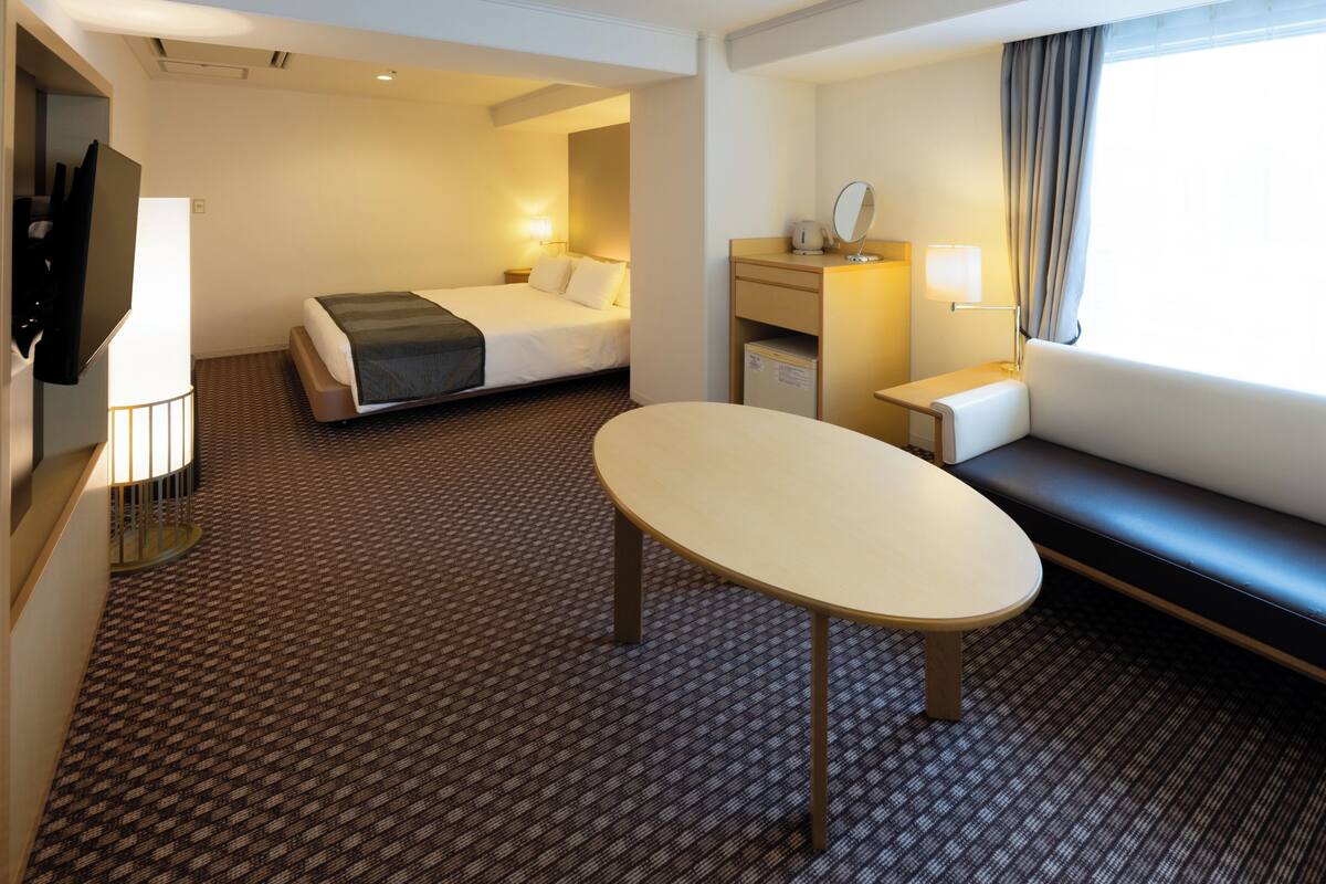A hotel room with a bed, a desk, a chair, a TV, and a window with curtains.