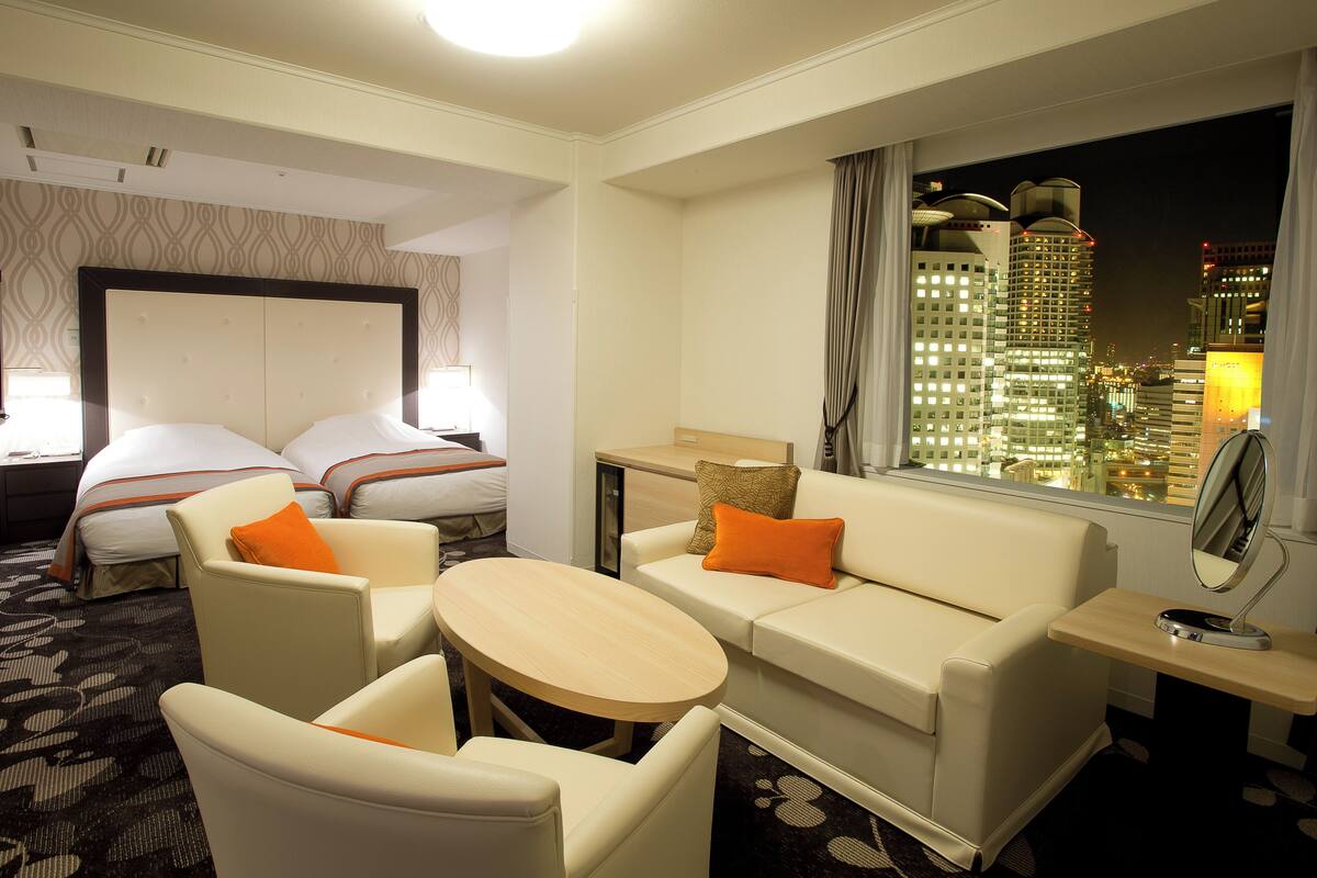 A hotel room with a bed, two armchairs, a sofa, a small table, and a window with a city view.