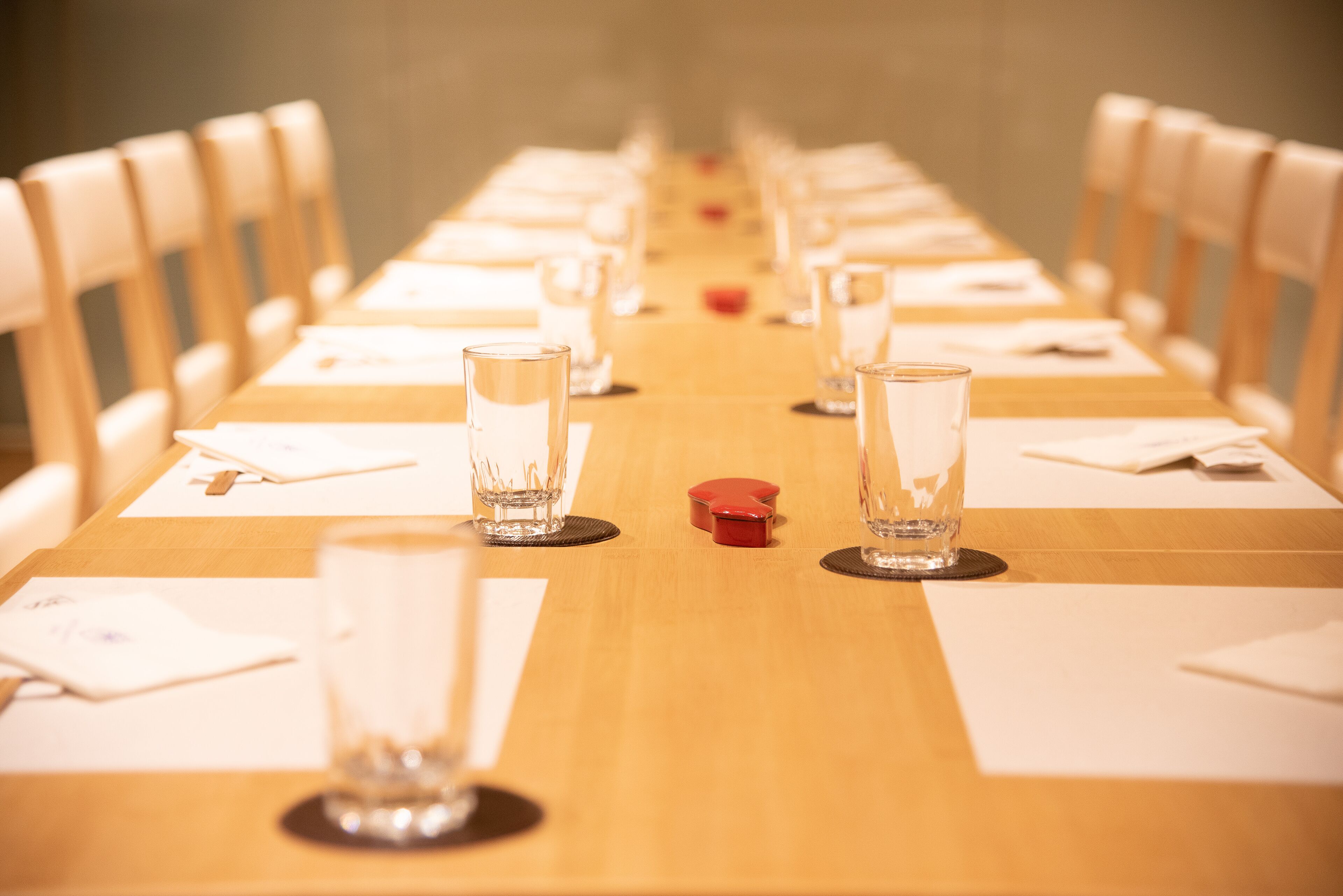 A long wooden table with chairs on both sides, set with clear glasses and white napkins.