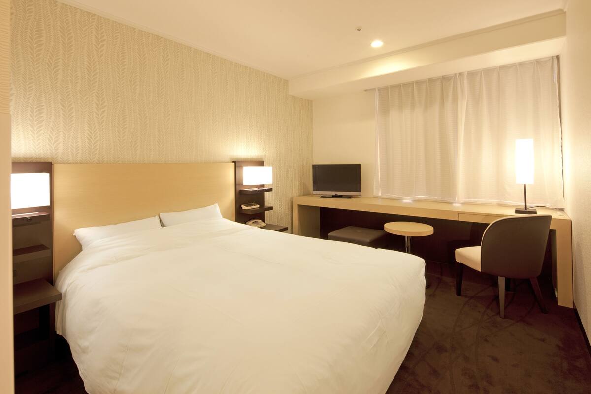 A hotel room with a large bed, a desk with a computer, a chair, and a TV.