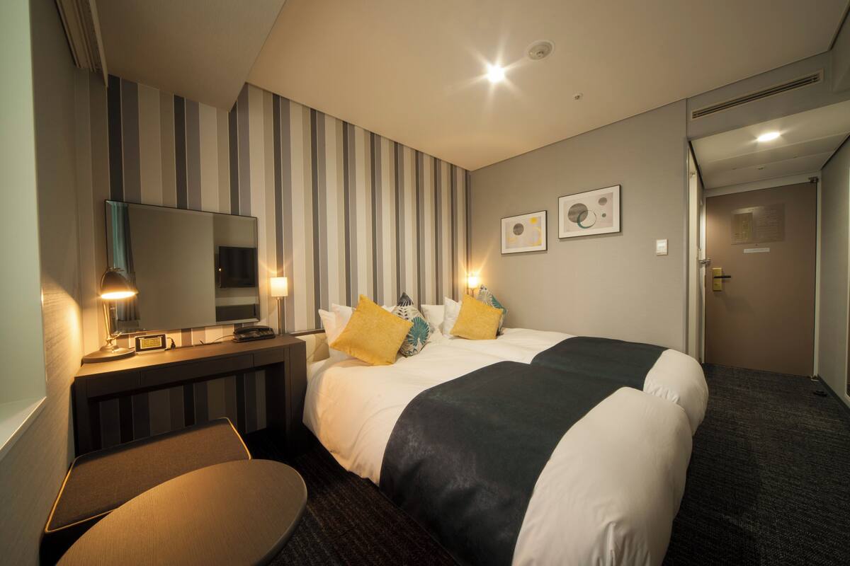 A hotel room with a bed, bedside table, lamp, and a mirror.