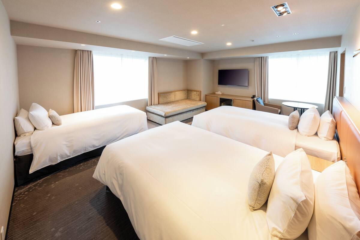 A hotel room with two single beds, a sofa bed, a TV, and a small table.