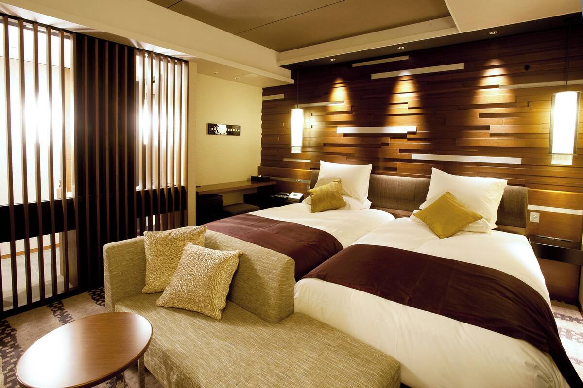 A modern hotel room with a large bed, a sofa, a small table, and a wooden partition.