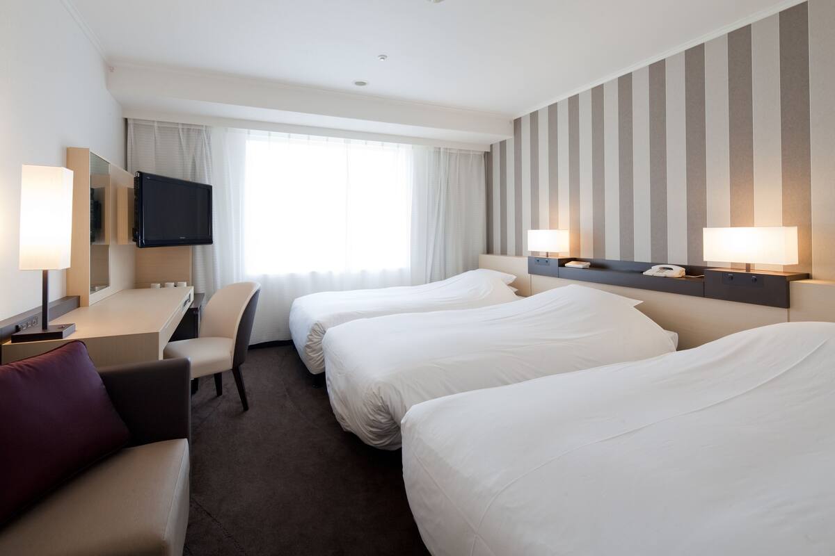 A hotel room with two beds, a desk, a chair, a TV, and two bedside lamps.
